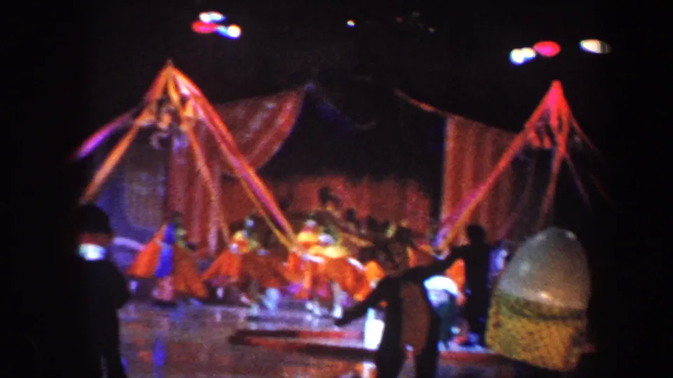 Circus performers in orange and blue costumes appear near a tent-like set piece in grainy 1960 Baltimore home-movie footage.