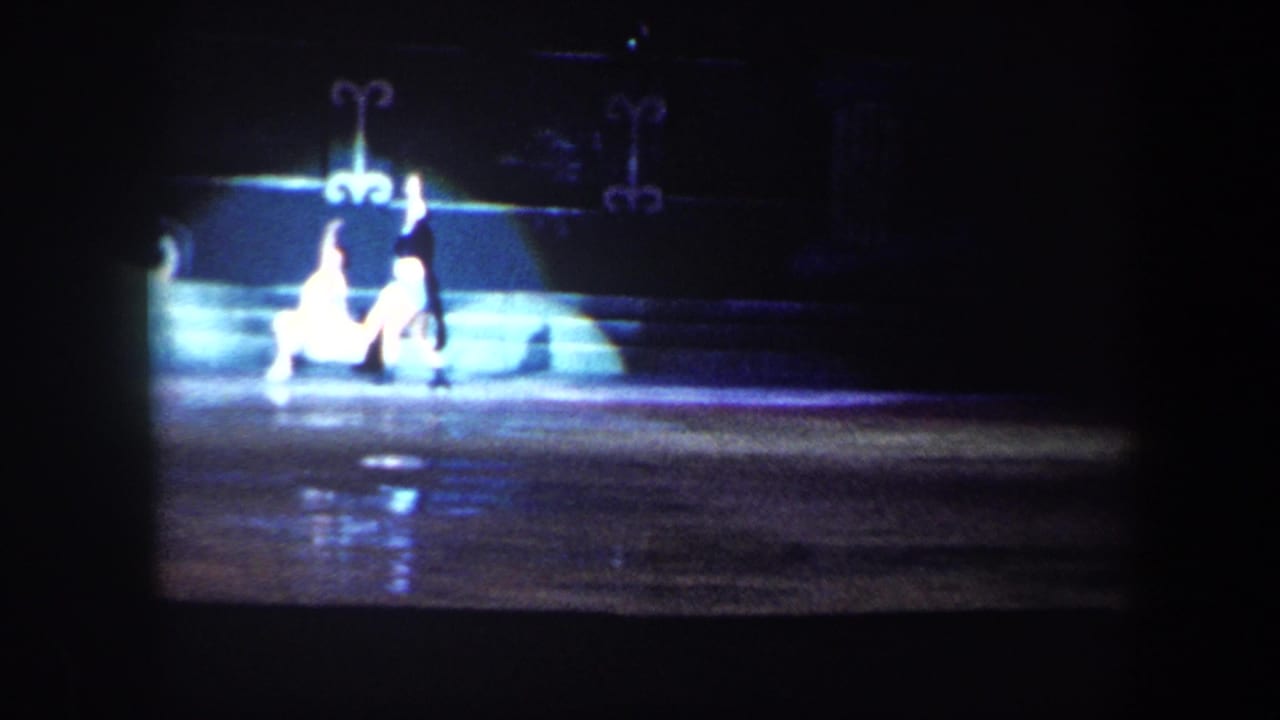 Spotlighted skater on an ice rink with another figure nearby in darkness.