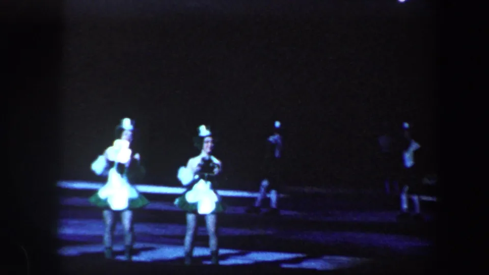 A group of costumed skaters appears under theatrical lights during the 1960 Baltimore ice show footage.