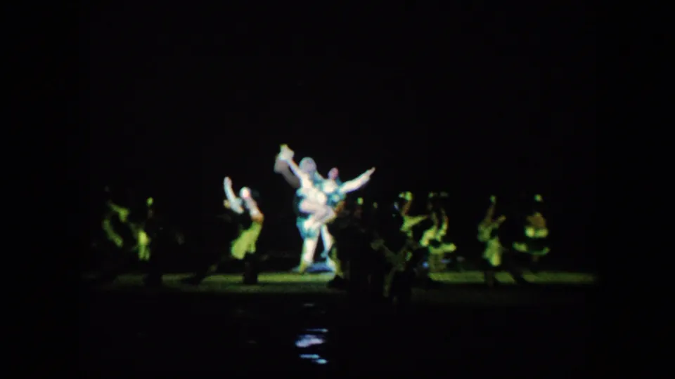 The ice show builds to an ensemble moment with a central lifted pose and surrounding performers in greenish stage light.