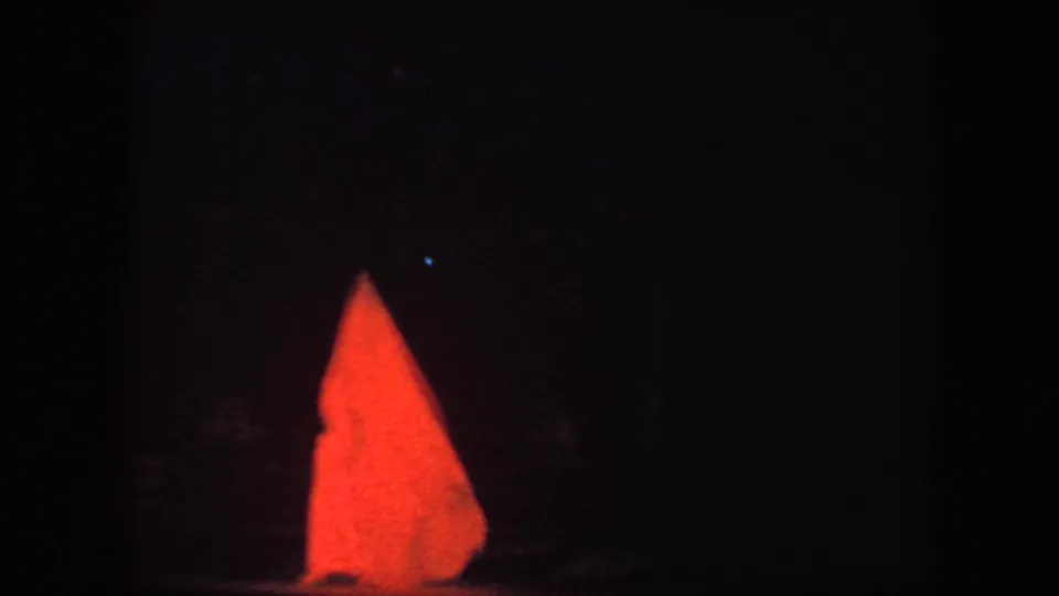 Low-light 8mm frame from the Baltimore ice show, with red illuminated triangular scenic pieces dominating the dark rink view.