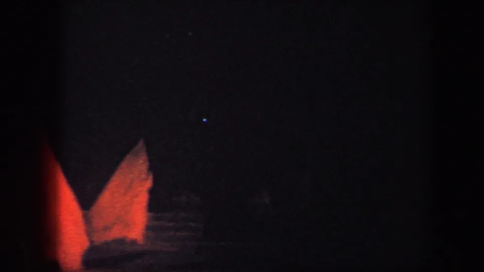 Baltimore 1960 home-movie frame showing red lit scenic pieces on a dark ice-show rink, with only faint background detail visible.
