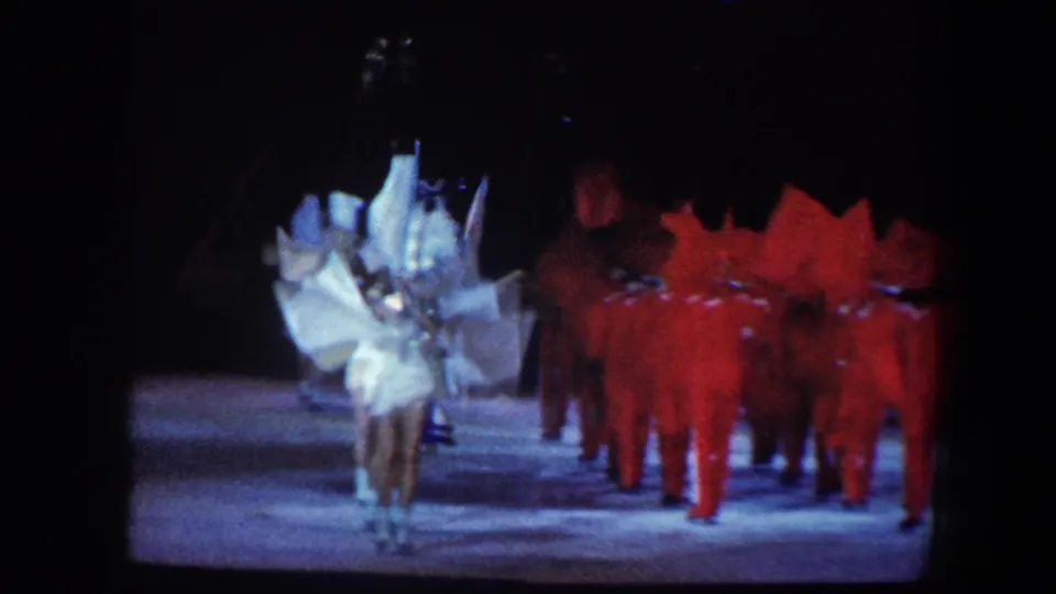 1960 Baltimore 8mm frame showing a stage ensemble with a white feathered performer and a group in red costumes.