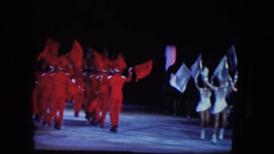 1960 Baltimore 8mm frame showing red-costumed ensemble dancers and white-costumed performers on a dark stage.