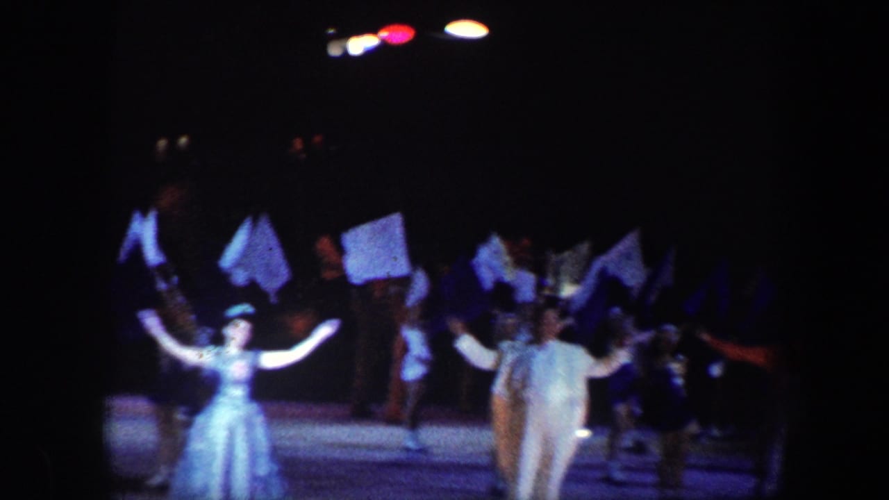 1960 Baltimore 8mm frame showing performers in costumes raising flags on a dark stage under colored spotlights.