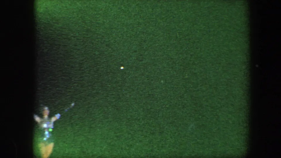 Green-shifted 8mm frame from the Baltimore stage performance, with a partially visible costumed performer near the lower edge.