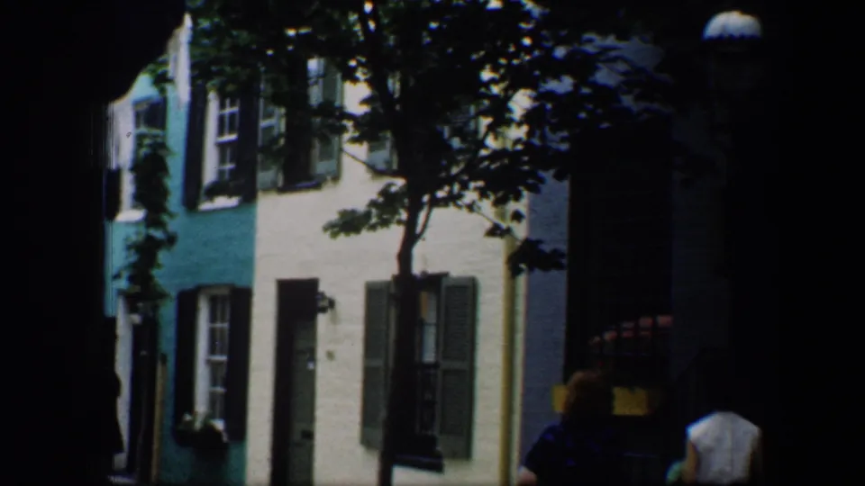 The women move toward the right edge of a Baltimore street view, with painted row-house facades, shutters, trees, and shadows visible.