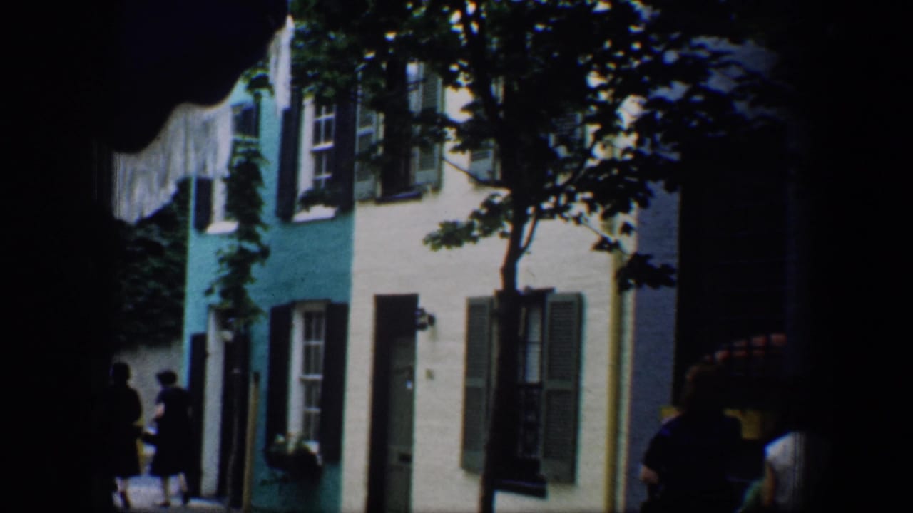 Painted row houses with shutters and pedestrians under street trees.