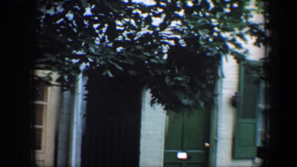 1960 Baltimore frame showing a green door, green shutters, shaded siding, and a neighboring doorway partly at the edge of view.