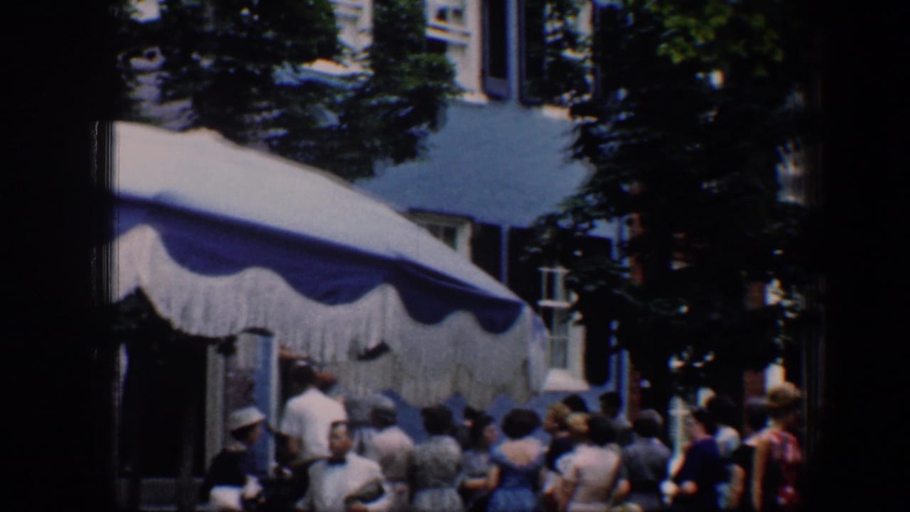 People standing near a scalloped awning with trees and building windows behind them.