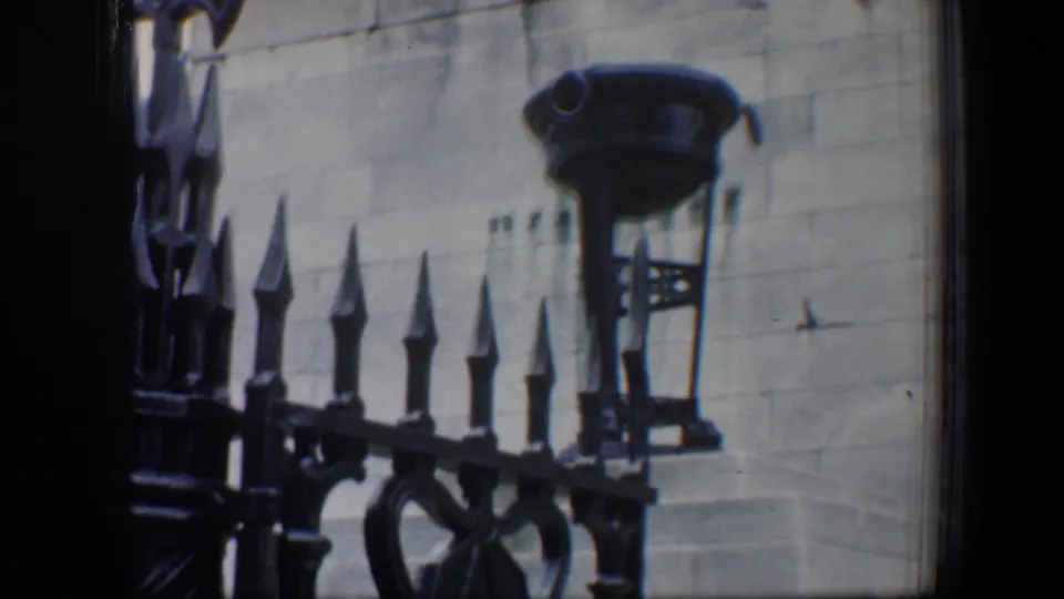 1960 Baltimore detail of black wrought iron fencing, pointed finials, and a wall-mounted lamp on a light stone facade.