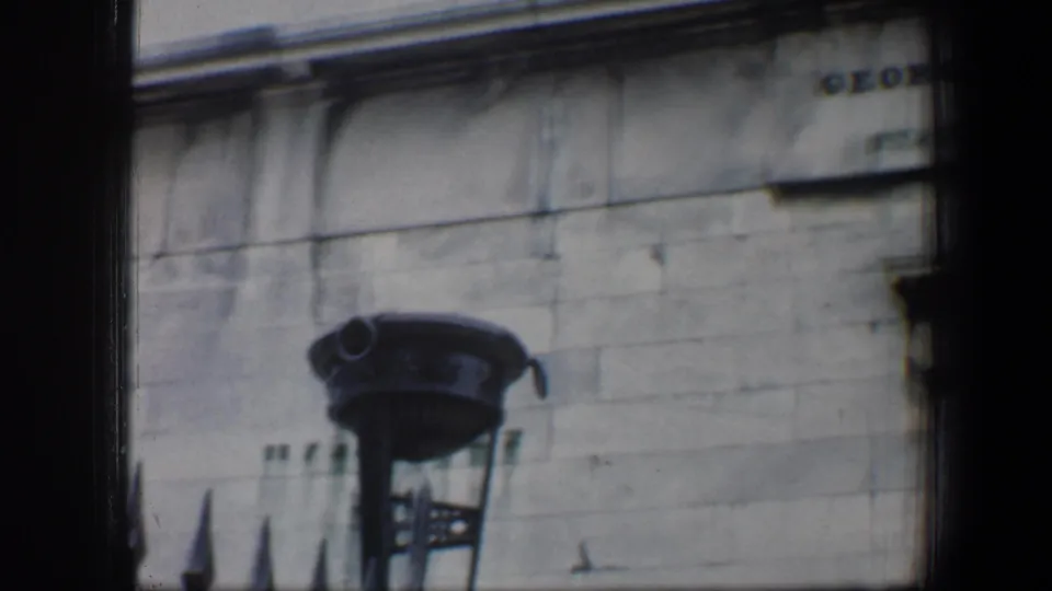 The camera frames a decorative lamp on a stone facade, with part of the dedication plaque entering at the upper right.