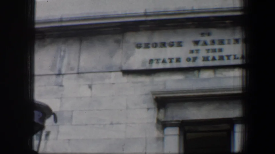 A Baltimore stone building facade shows part of the George Washington dedication plaque above a doorway surround.