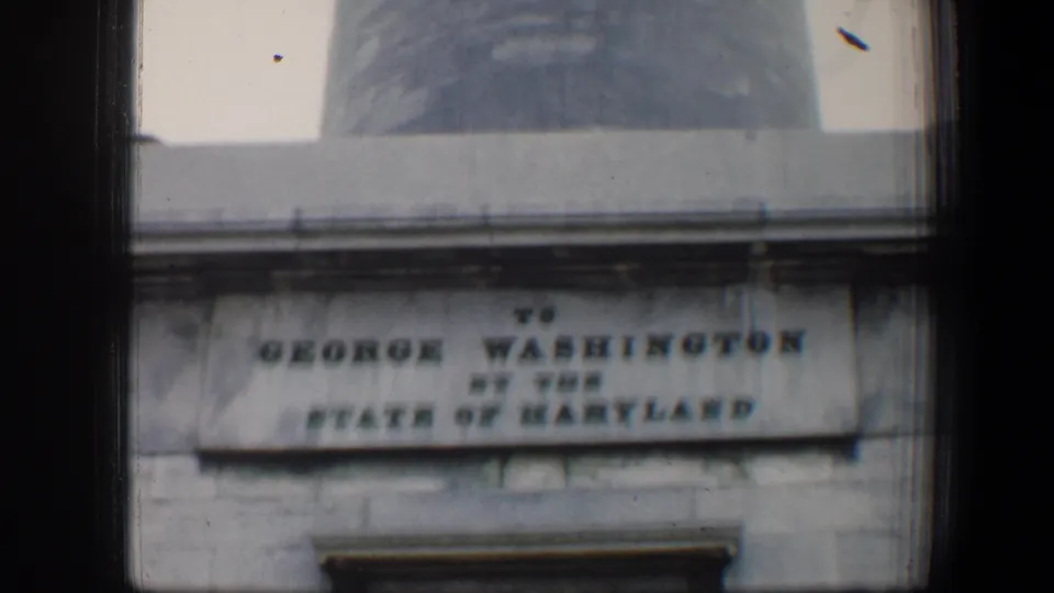 1960 Baltimore 8mm frame showing the George Washington Monument inscription at the stone base with the obelisk rising above.