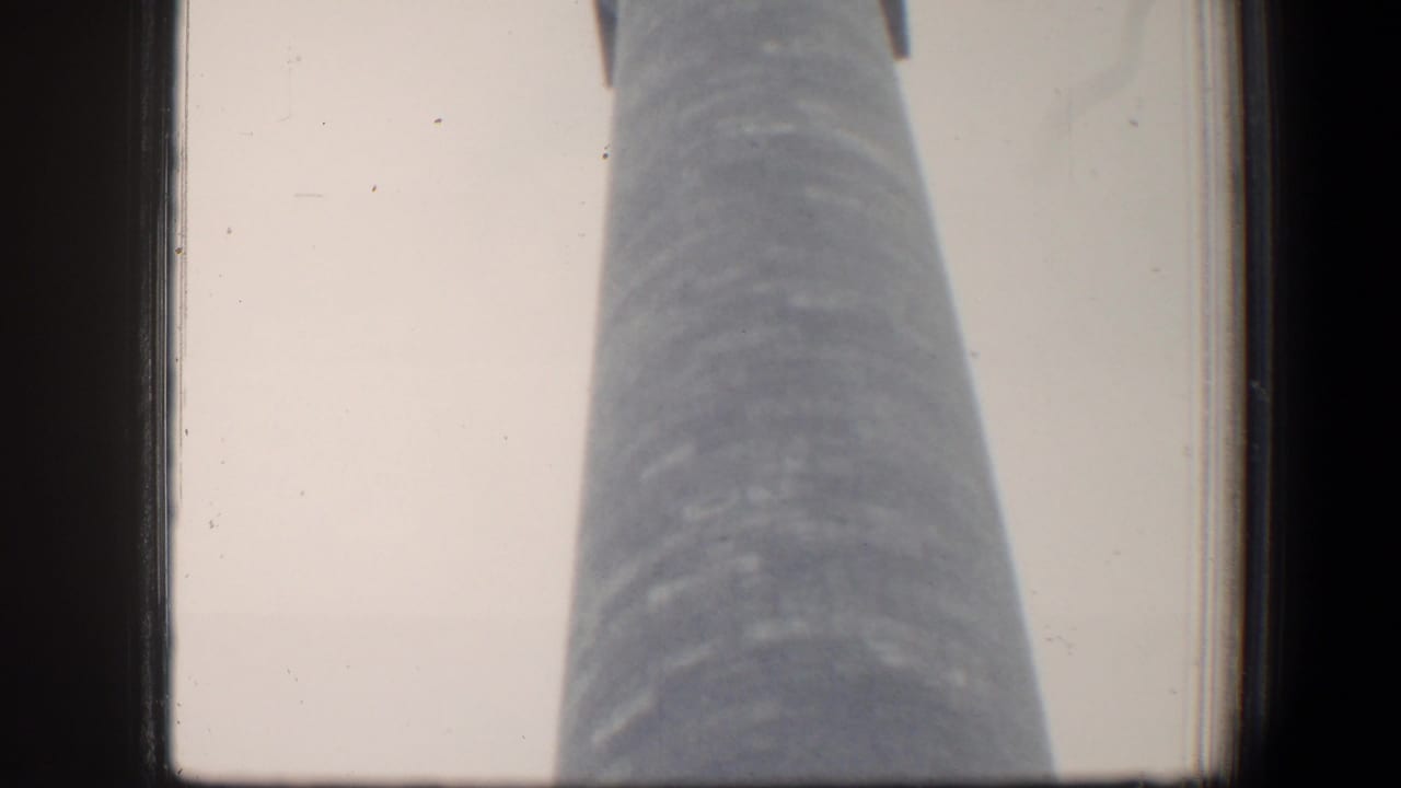 Low-angle view up a tall cylindrical monument with a square top against pale sky.