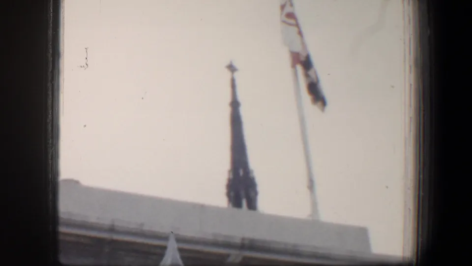 1960 Baltimore home-movie frame showing a distant steeple, rooftop edge, and flag near the monument area.