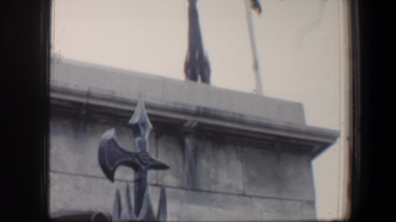 Stone monument base behind a decorative black fence, partly framed by dark film edges.