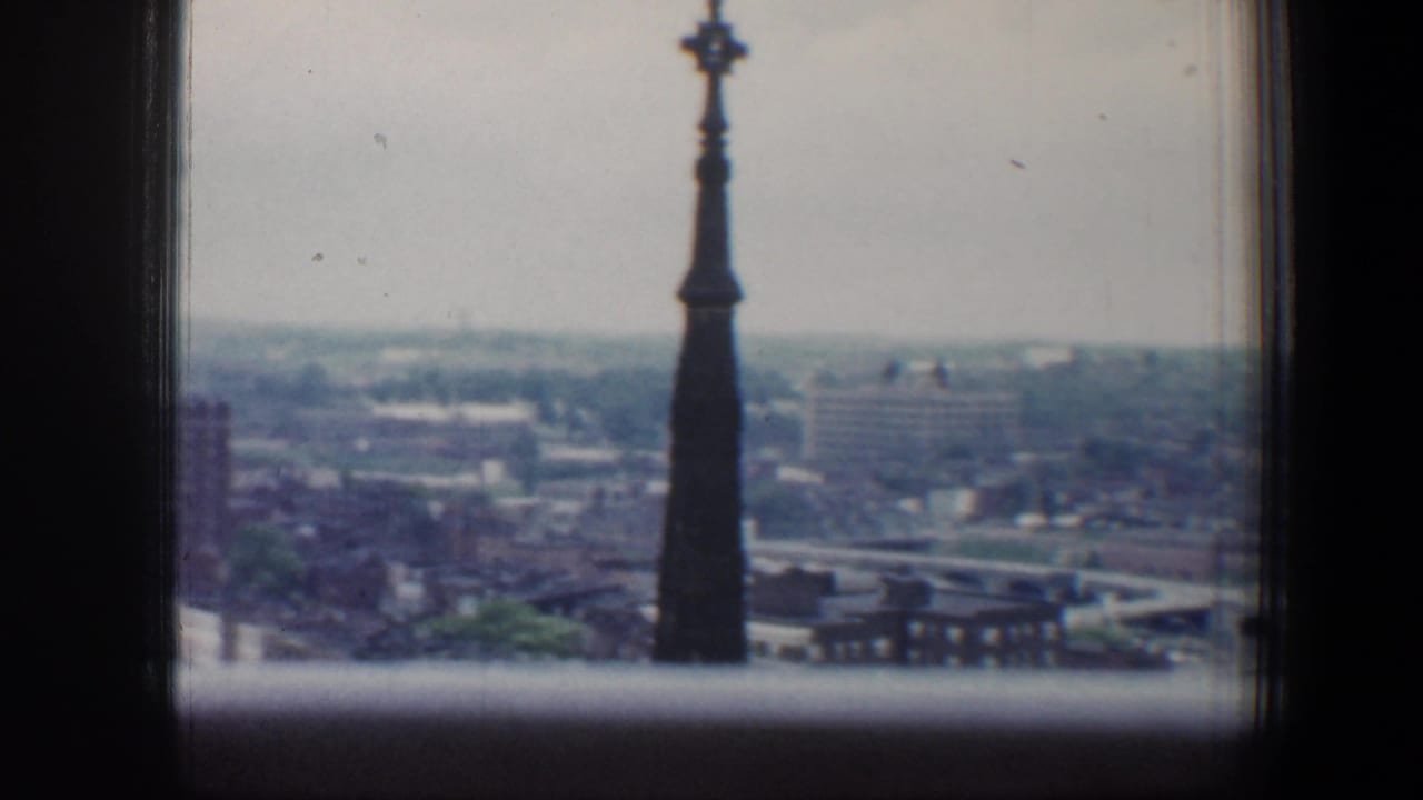 Dark spire framed by a window above a hazy city skyline.