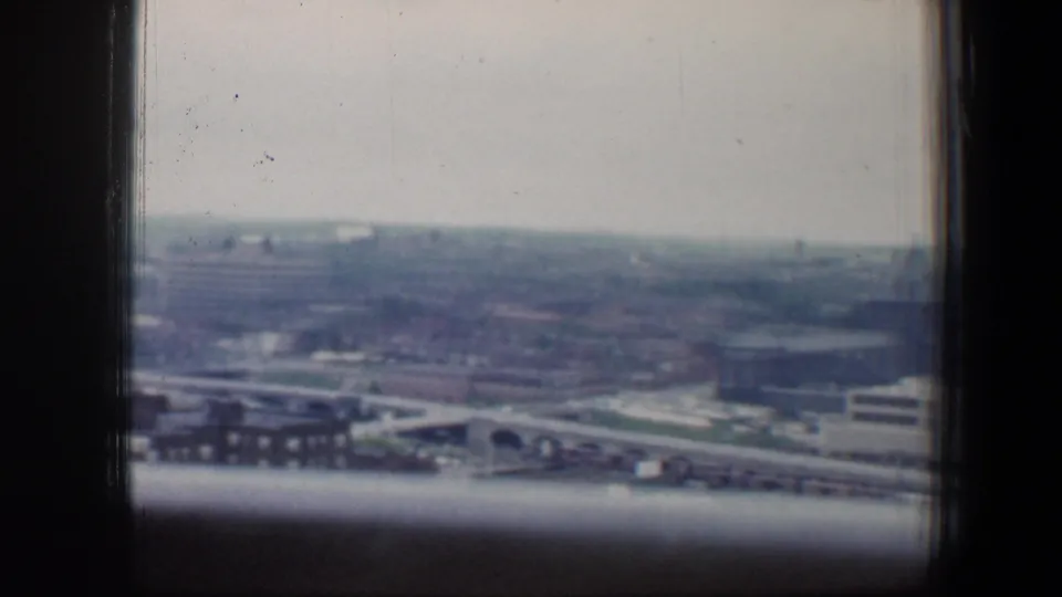Baltimore cityscape in 1960 viewed through window panes, showing rooftops, roadways or bridges, and a soft overcast horizon.