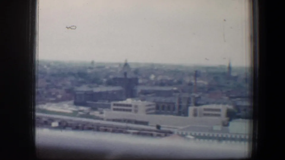 A soft 1960 Baltimore skyline frame with block-like buildings, a distant spire, rooftops, and a pale overcast sky.