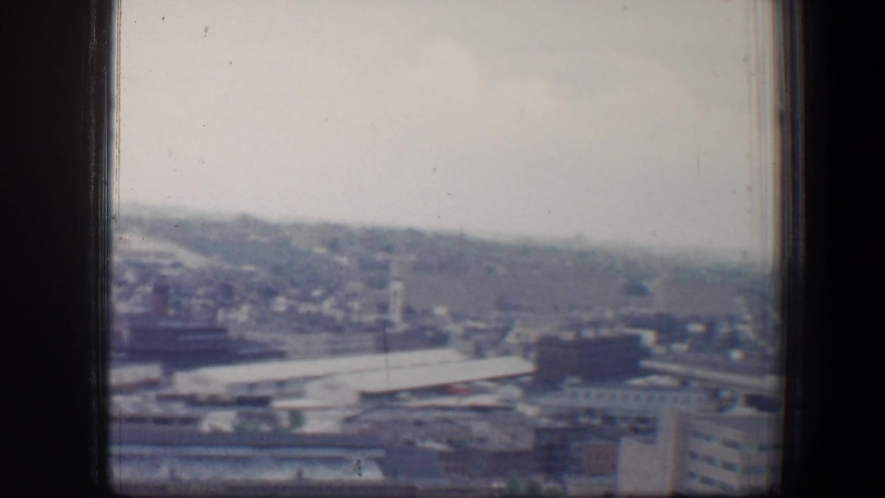 Hazy cityscape seen through dark window framing from a high vantage point.
