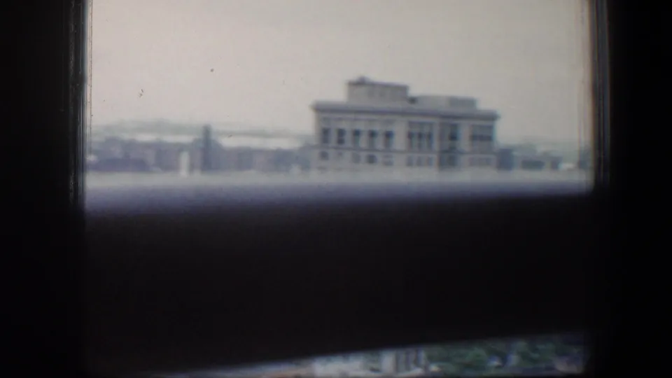 1960 Baltimore view with a large institutional-looking building, a distant steeple, rooftops, and dark framing across the foreground.