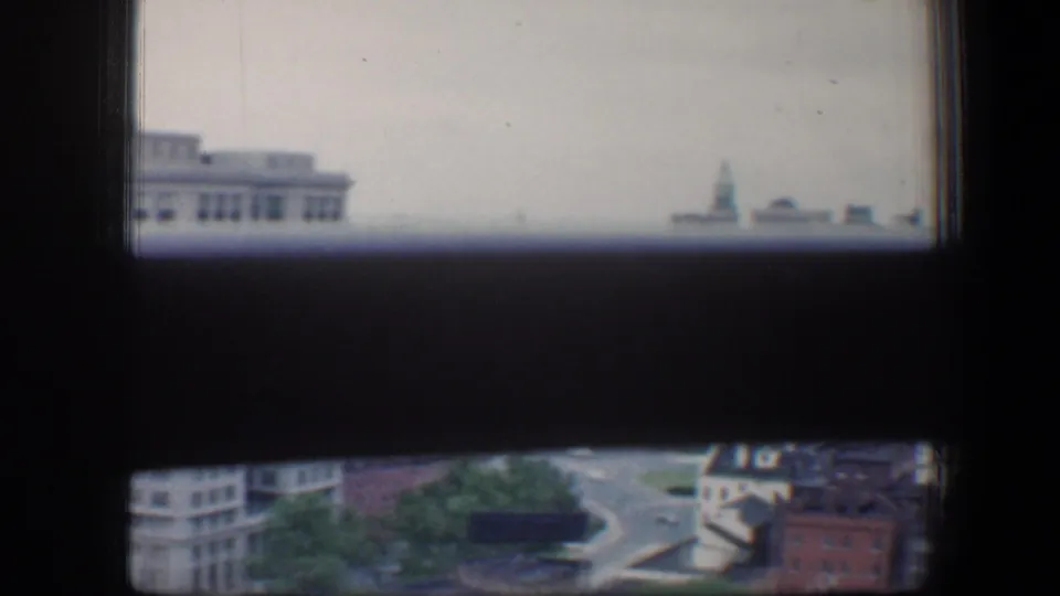 Baltimore city view from 1960 framed by dark window edges, showing a steeple, rooftops, a road, and low buildings below.