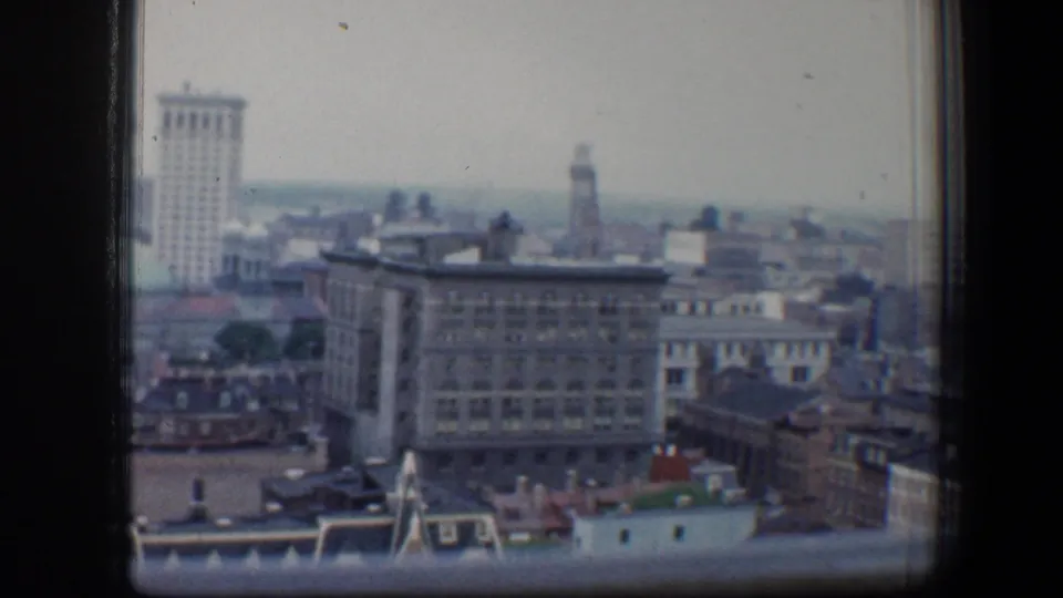 Window-framed 1960 Baltimore skyline view with older commercial buildings and taller structures beyond.