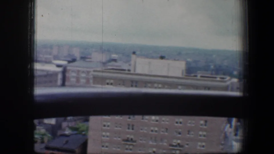 Lower right pane frames a Baltimore rooftop edge, brick facade, and hazy city distance in 8mm footage.