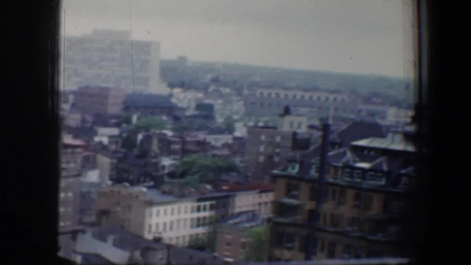 High-angle 1960 Baltimore view with older rooflines, brick structures, distant streets, and a dark window frame at the edge.