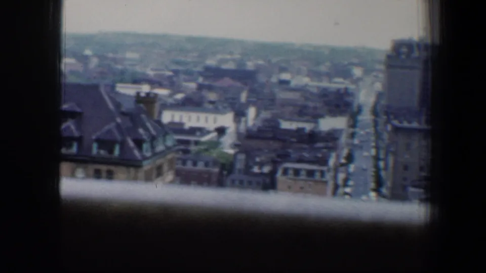High-angle 1960 Baltimore cityscape framed by window mullions, showing rooftops, streets, and layered urban buildings.