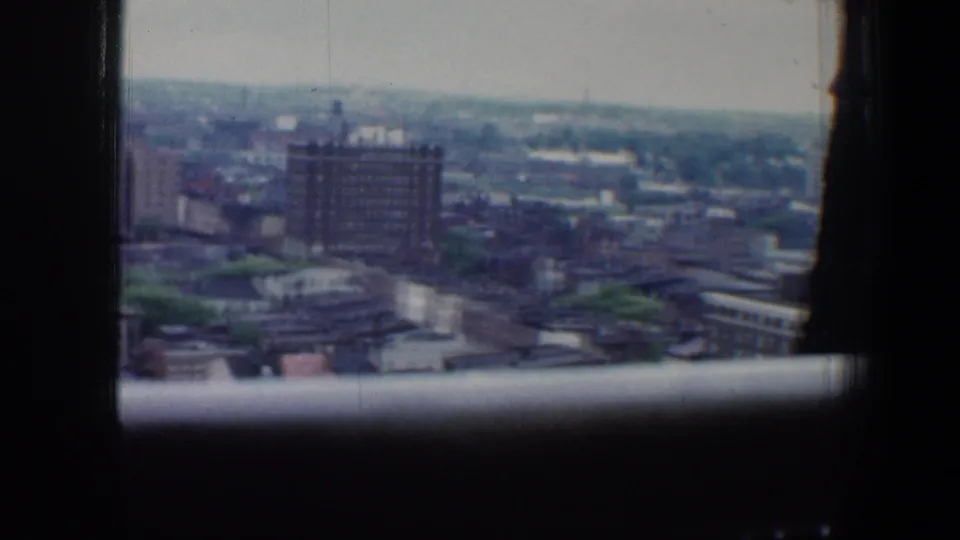 1960 Baltimore city view from a high vantage point, with soft distant buildings and dark window framing in the foreground.