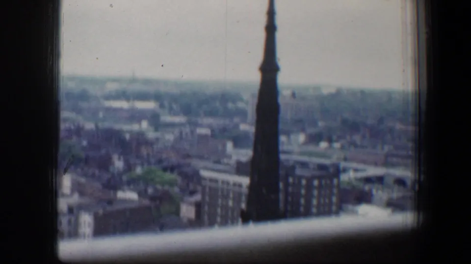 A tall church steeple stands near the foreground of a 1960 Baltimore cityscape with brick buildings and distant rooftops.