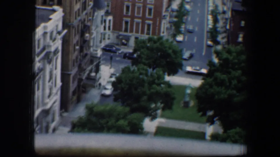 An elevated 1960 Baltimore view looks down on a tree-lined street with parked cars, brick buildings, sidewalks, and a small green lawn.