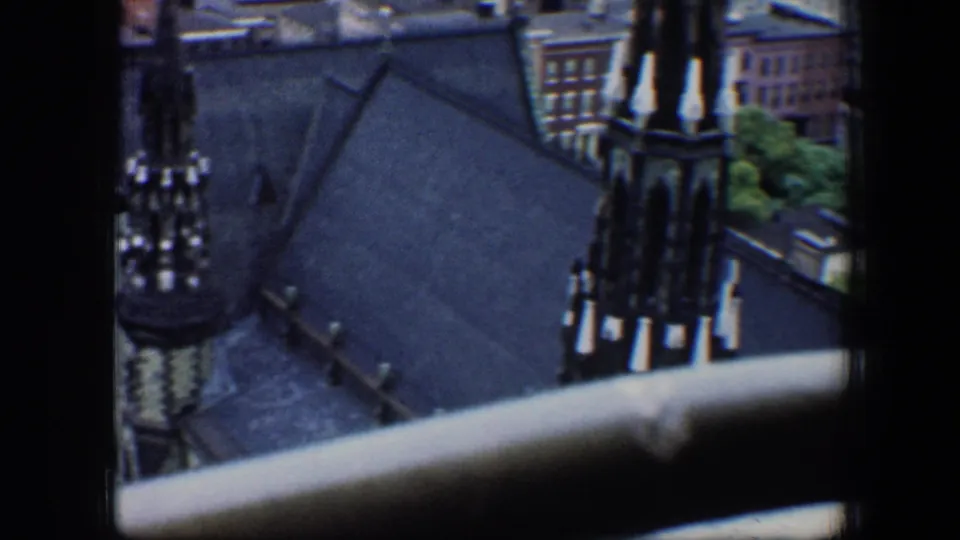 1960 Baltimore home-movie frame showing a church or cathedral roof and spire from a high window, with buildings behind.