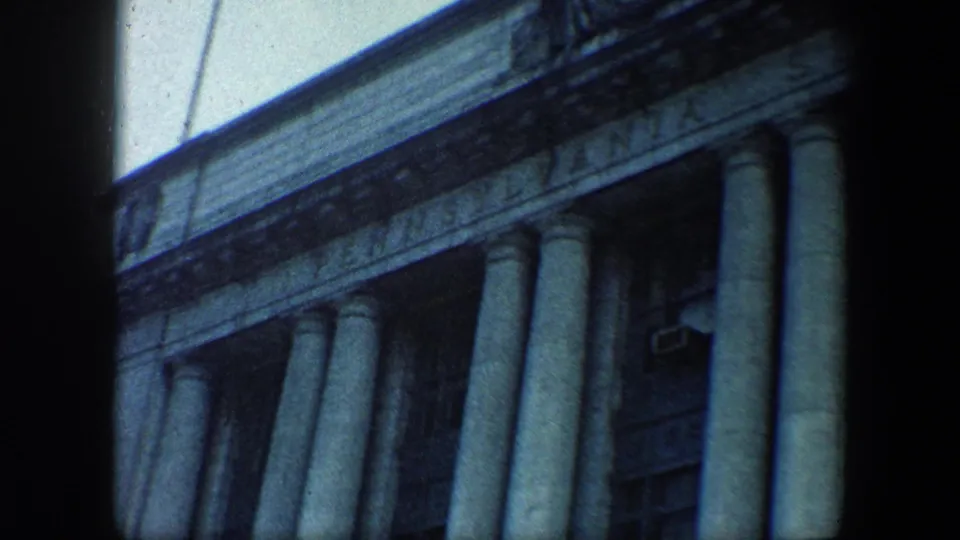 Home-movie frame of Baltimore architecture, showing a long row of columns and soft blue-green 8mm color.