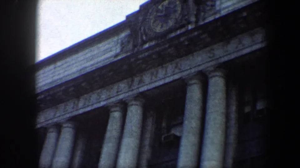 1960 Baltimore 8mm frame showing partial station lettering, carved stonework, tall columns, and a window air conditioner.