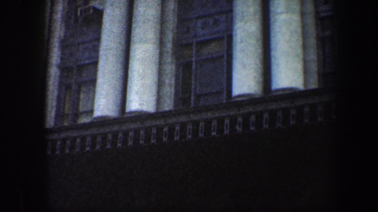 Upper facade of a dark stone building with tall columns and windows at dusk.