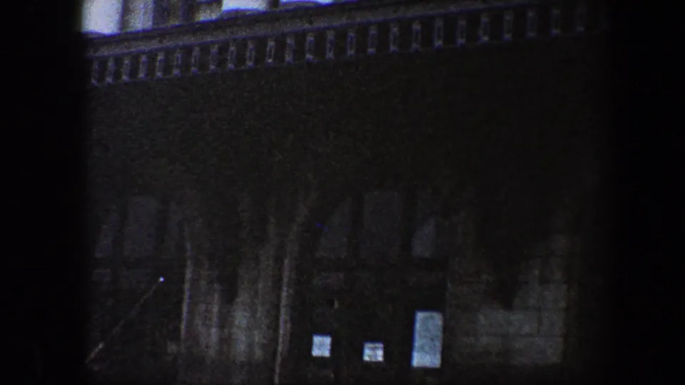 Low-light 1960 Baltimore exterior showing a large stone facade with windows above and posted notices near recessed lower doors.