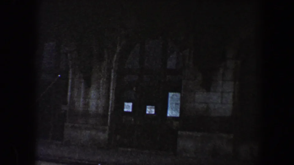 1960 Baltimore 8mm frame of the lower facade, showing arched stone details, dark entrance areas, steps, railings, and posted notices.