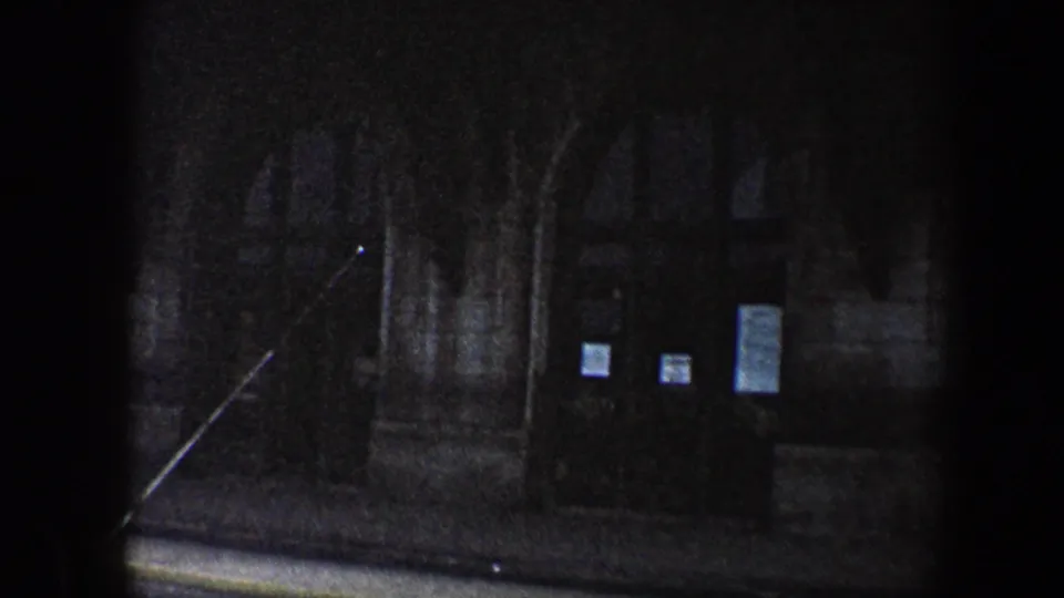 Final 1960 Baltimore 8mm frame on the shadowed lower entrance of a large stone building with arches, railings, steps, and notices.