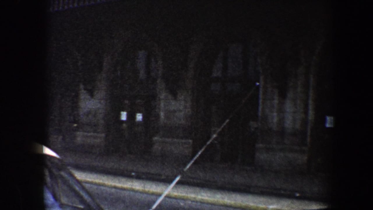 Night street facade with curb, building entrance, and a diagonal foreground line.
