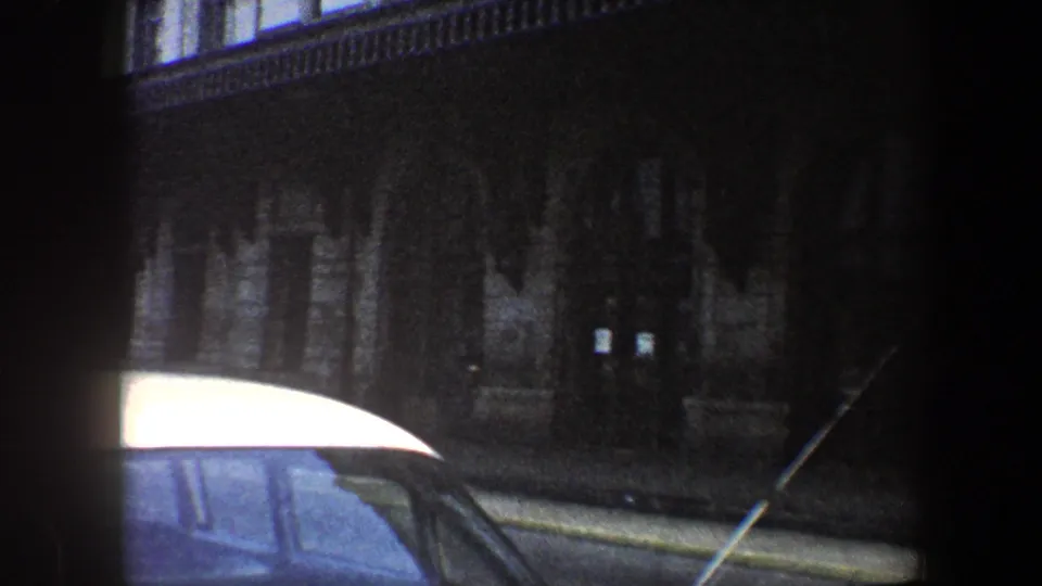 1960 Baltimore street view with the roof of a white parked car in front of a dark masonry building.