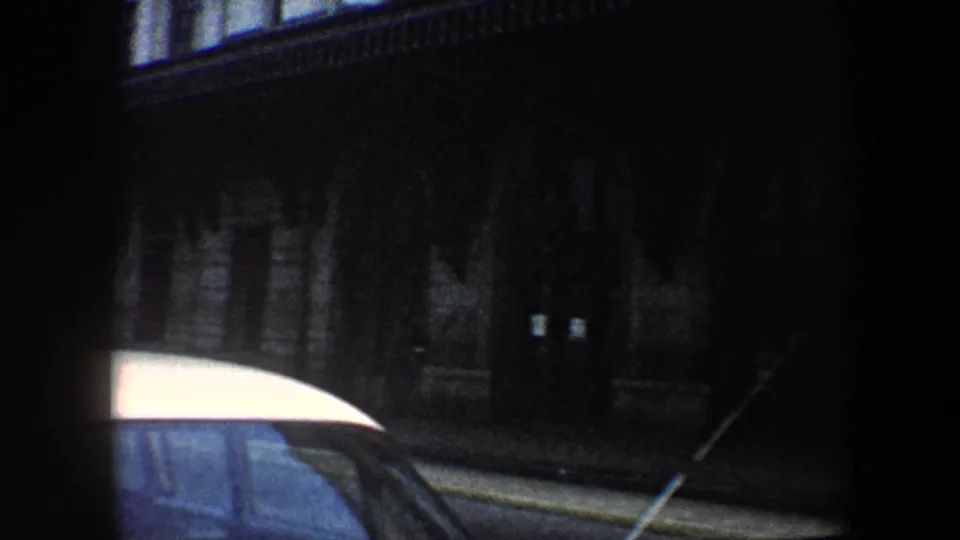 1960 Baltimore street view from a vehicle, with a white-roofed car partly blocking a dark museum entrance.