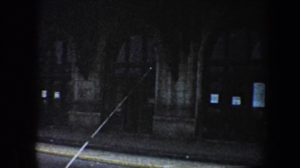 Grainy 1960 Baltimore frame showing a shadowed arched entrance, posted notices, and a stone institutional facade.