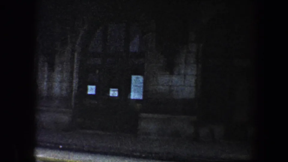 1960 Baltimore 8mm frame of a museum-like stone entrance with posted notices, steps, and deep shadows.