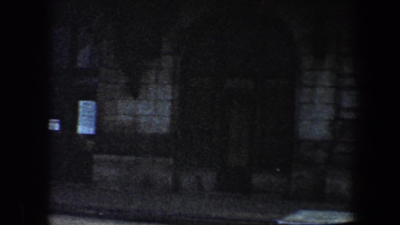 Dim stone building exterior with dark doorway and small posted notices.