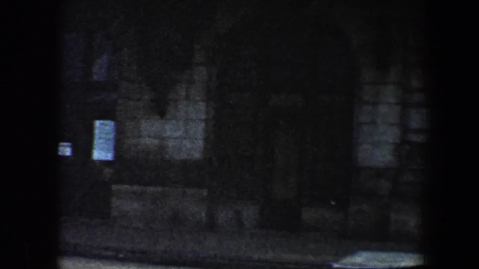 1960 Baltimore 8mm frame showing a dim grey stone facade with a dark doorway and small posted signs.