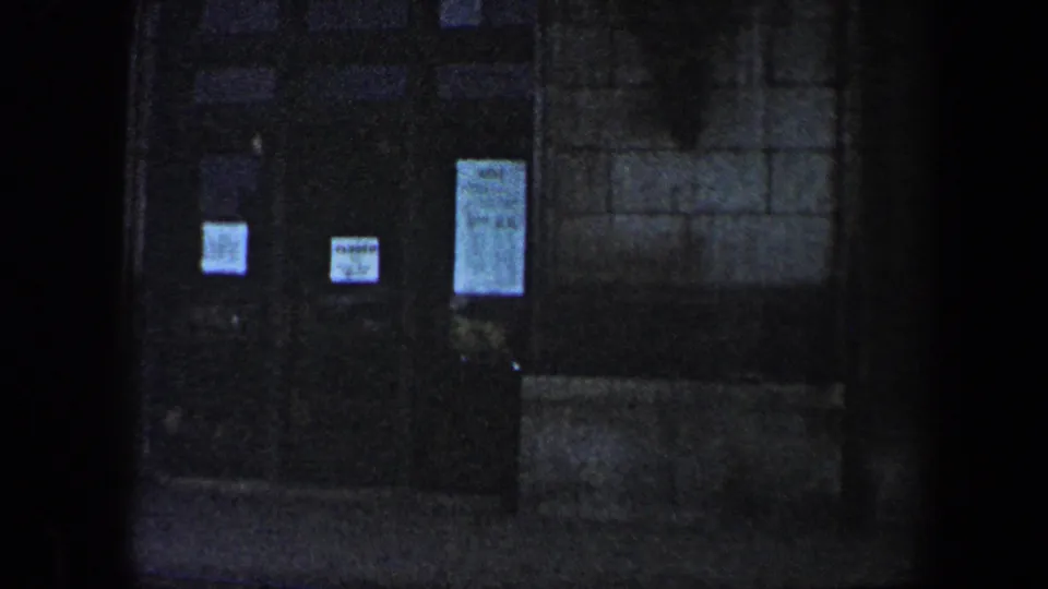 1960 Baltimore 8mm view of dark building doors with several posted notices on a dim stone exterior.