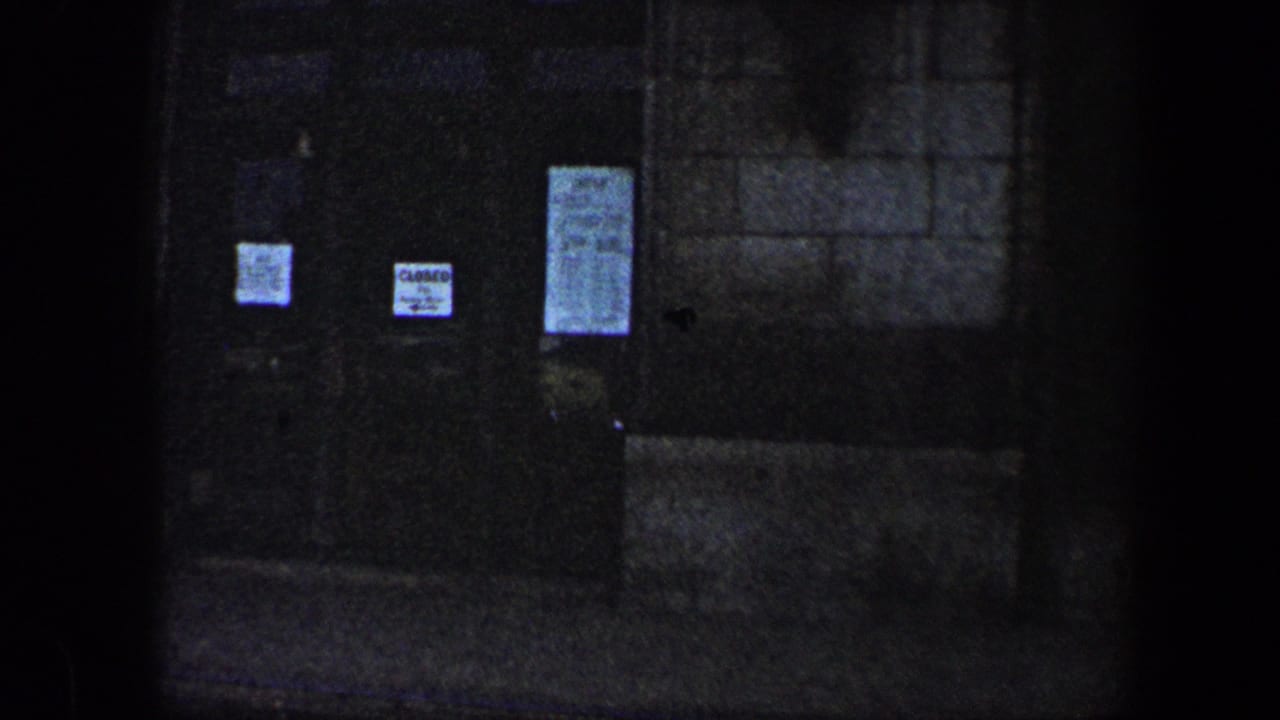 Dim 1960 Baltimore exterior view of a dark doorway with several paper notices posted on the doors.